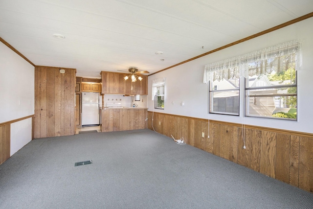 12963 E Englewright Dr, Sand Lake, MI 49343 - unfurnished living room featuring ornamental molding, wooden walls, light carpet, a wainscoted wall, and a ceiling fan