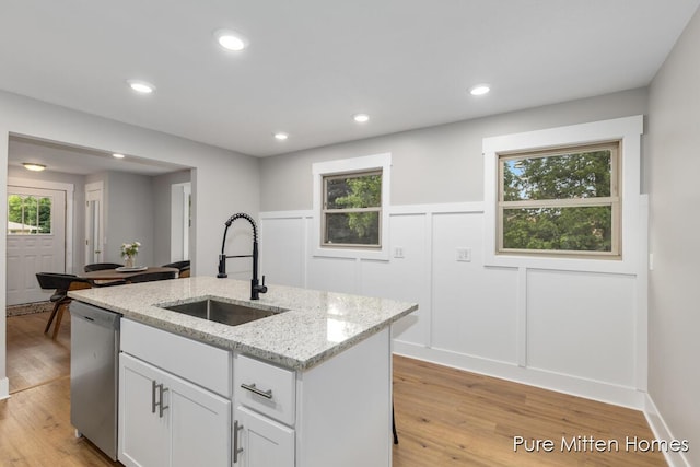 630 Westview Ave NW, Grand Rapids, MI 49504 - kitchen featuring stainless steel dishwasher, light wood-style floors, white cabinets, a kitchen island with sink, and light stone countertops