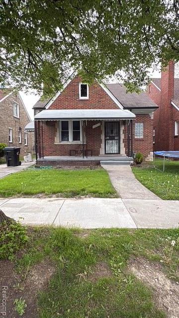19715 Spencer St, Detroit, MI 48234 - bungalow featuring a trampoline, brick siding, a front yard, and covered porch