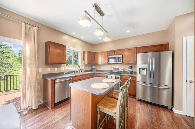 440 Shiloh Dr, Chelsea, MI 48118 - kitchen with appliances with stainless steel finishes, dark wood-style flooring, brown cabinetry, pendant lighting, and a kitchen island