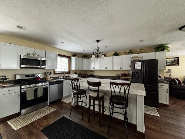 313 N Matteson St, Bronson, MI 49028 - kitchen featuring appliances with stainless steel finishes, a textured ceiling, a kitchen bar, white cabinets, and dark countertops