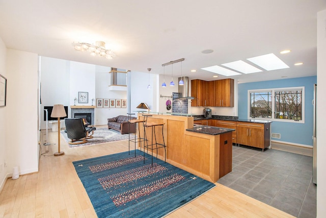 8023 Trail Rdg, Dexter, MI 48130 - kitchen with wall chimney exhaust hood, a skylight, brown cabinetry, a glass covered fireplace, and a kitchen bar