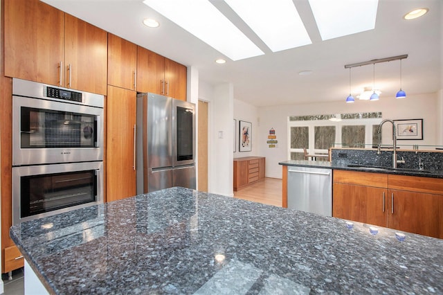 8023 Trail Rdg, Dexter, MI 48130 - kitchen with stainless steel appliances, a skylight, brown cabinets, dark stone counters, and recessed lighting
