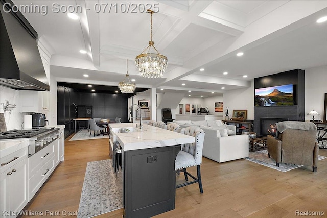 6295 Canter Creek Trl, Grand Blanc, MI 48439 - kitchen featuring wall chimney range hood, stainless steel gas stovetop, a warm lit fireplace, a chandelier, and light wood-style flooring