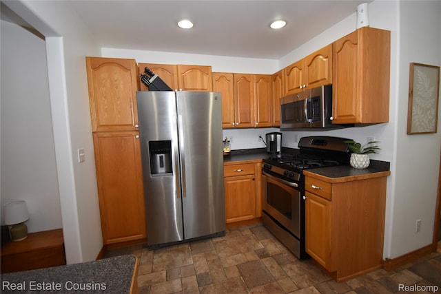 116 Park St, Gaines, MI 48436 - kitchen featuring appliances with stainless steel finishes, dark countertops, dark stone finish floors, brown cabinetry, and recessed lighting