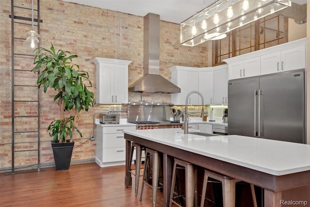 127 S Union St, Traverse City, MI 49684 - kitchen featuring wall chimney range hood, built in refrigerator, brick wall, wood finished floors, and white cabinetry