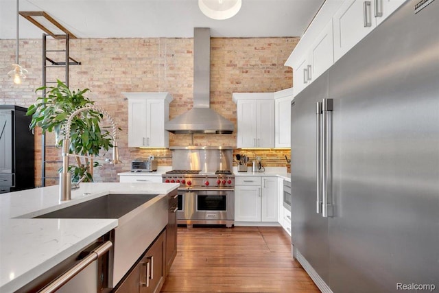 127 S Union St, Traverse City, MI 49684 - kitchen with high quality appliances, wall chimney exhaust hood, brick wall, light stone countertops, and white cabinetry
