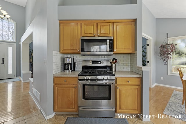6641 Laguna Vista Dr NE, Rockford, MI 49341 - kitchen featuring appliances with stainless steel finishes, light countertops, light wood finished floors, tasteful backsplash, and a chandelier