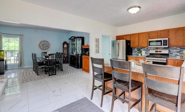 10895 Riley St, Zeeland, MI 49464 - kitchen featuring stainless steel appliances, brown cabinetry, light marble finish floors, and backsplash