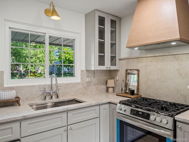 3025 Clawson Ave, Royal Oak, MI 48073 - kitchen featuring custom range hood, stainless steel gas range oven, glass insert cabinets, decorative backsplash, and white cabinetry