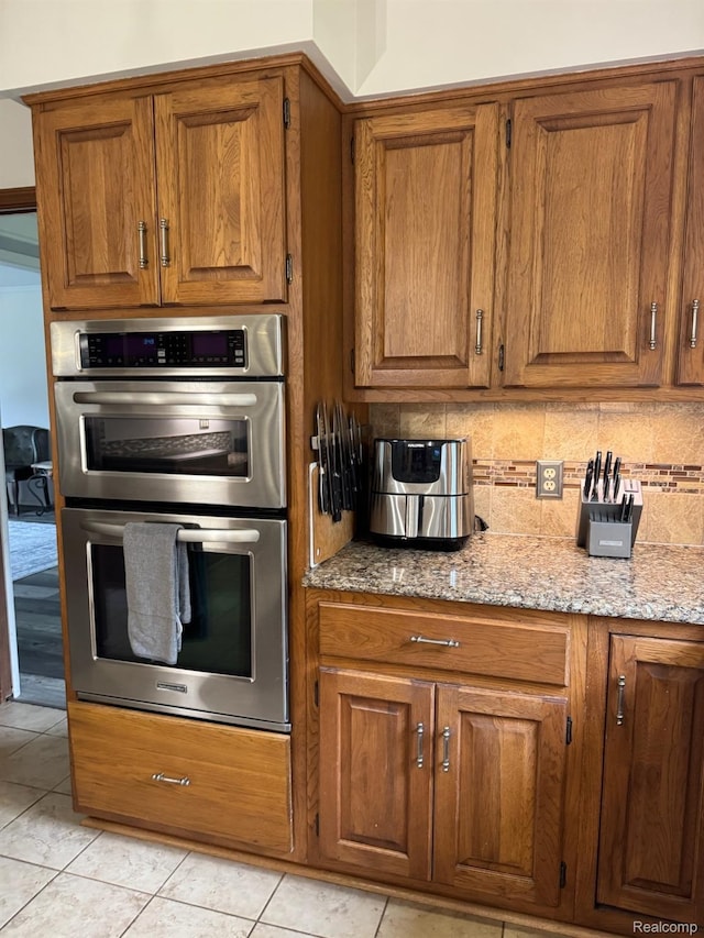 472 Ashton Ct SE, Grand Rapids, MI 49546 - kitchen with double oven, brown cabinetry, backsplash, light stone counters, and light tile patterned flooring