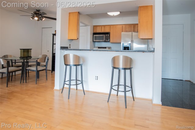 3559 Port Cove Dr Unit 25, Waterford, MI 48328 - kitchen featuring appliances with stainless steel finishes, a ceiling fan, a kitchen breakfast bar, light wood-style floors, and dark countertops