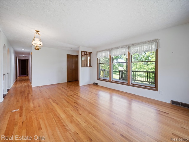 3225 W Marr Rd, Howell, MI 48855 - spare room with a textured ceiling, light wood finished floors, a chandelier, and arched walkways