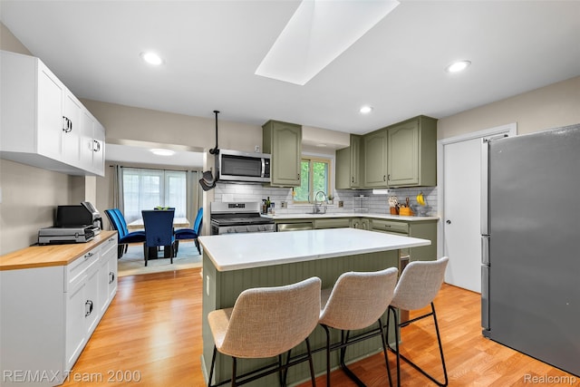 30695 Lyndon St, Livonia, MI 48154 - kitchen featuring green cabinets, appliances with stainless steel finishes, backsplash, a kitchen breakfast bar, and light wood finished floors