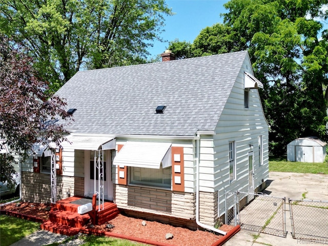 329 Bede St, Otisville, MI 48507 - view of front of home featuring roof with shingles, a gate, a chimney, stone siding, and a storage unit