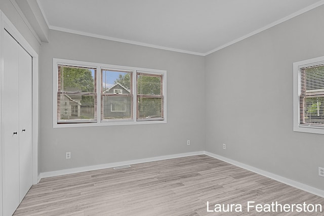 1119 White Ave NW, Grand Rapids, MI 49504 - unfurnished bedroom featuring light wood-type flooring, multiple windows, crown molding, and a closet