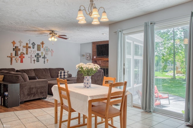279 Ardelean Dr, Owosso, MI 48867 - dining area featuring light tile patterned floors, a textured ceiling, a ceiling fan, a chandelier, and a fireplace
