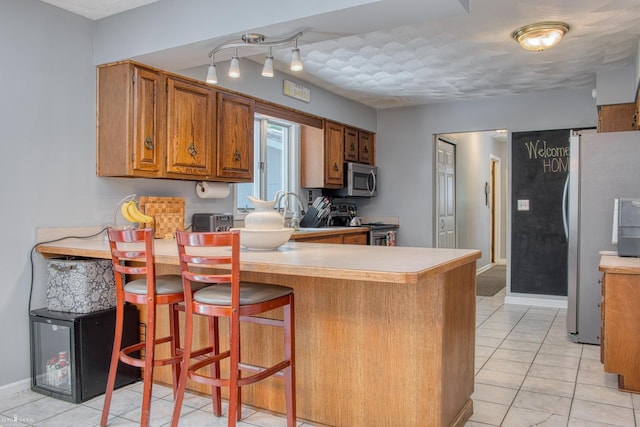 279 Ardelean Dr, Owosso, MI 48867 - kitchen with stainless steel appliances, brown cabinetry, a peninsula, and light countertops