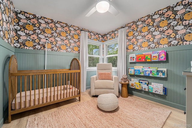 5690 Corunna Ave, Clarkston, MI 48346 - bedroom featuring wallpapered walls, a crib, a wainscoted wall, wood finished floors, and a ceiling fan