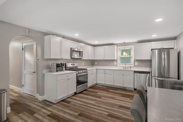 6590 Swartout Rd, Clay, MI 48001 - kitchen featuring appliances with stainless steel finishes, wood finished floors, light countertops, white cabinetry, and arched walkways
