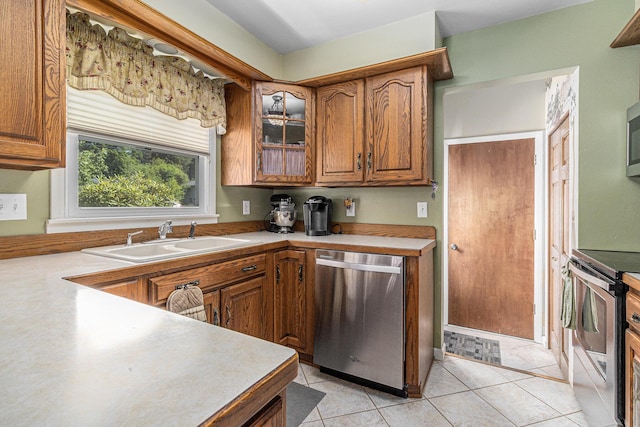 4650 Rollridge Ave, Kalamazoo, MI 49004 - kitchen featuring stainless steel appliances, brown cabinets, light countertops, light tile patterned floors, and glass insert cabinets