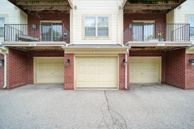 662 Village Ln, Milford, MI 48381 - view of front facade featuring a balcony, a garage, brick siding, and driveway