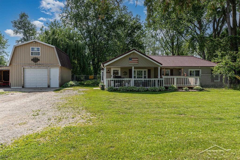 2370 S M-18 Hwy, Beaverton, MI 48612 - view of front facade with a garage, dirt driveway, an outdoor structure, a gambrel roof, and a metal roof