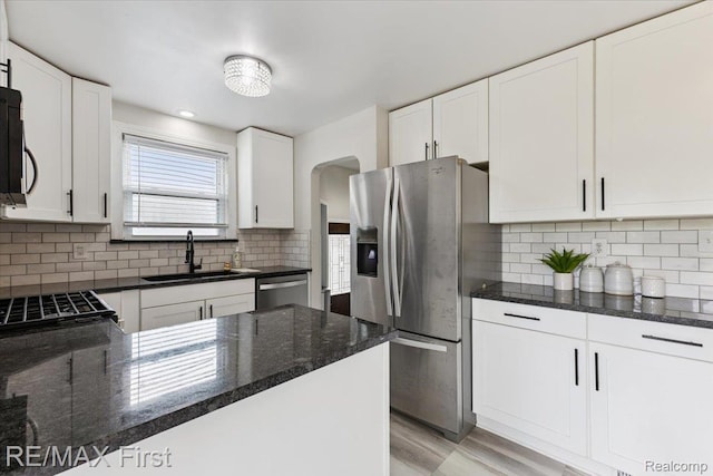 24360 Grove Ave, Eastpointe, MI 48021 - kitchen featuring stainless steel appliances, arched walkways, dark stone counters, white cabinets, and tasteful backsplash