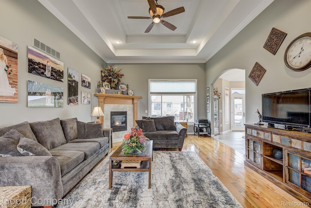 63705 Monticello E, Washington, MI 48095 - living room with ceiling fan, a tile fireplace, arched walkways, light wood-type flooring, and a raised ceiling