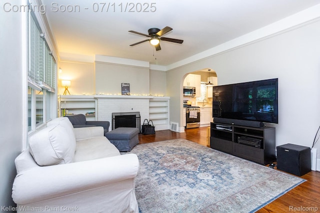 1424 Lakepointe St, Detroit, MI 48230 - living room featuring a brick fireplace, dark wood-style floors, ceiling fan, and arched walkways