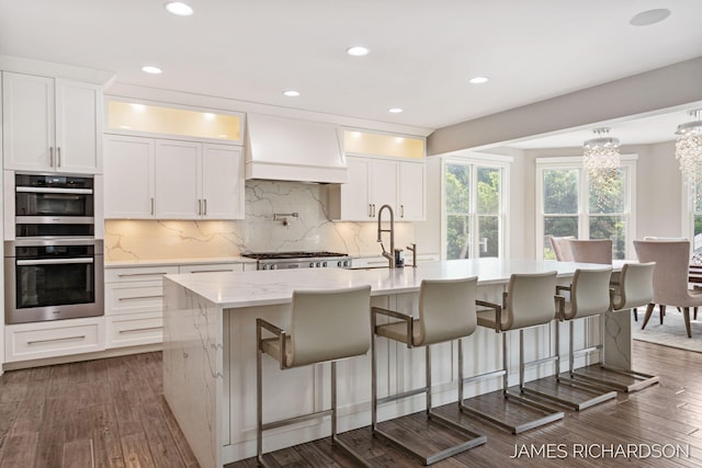 12974 Boulderway Trl, Grand Haven, MI 49417 - kitchen with appliances with stainless steel finishes, dark wood-type flooring, custom exhaust hood, backsplash, and an island with sink