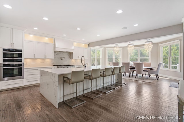 12974 Boulderway Trl, Grand Haven, MI 49417 - kitchen featuring dark wood-type flooring, premium range hood, double oven, decorative backsplash, and white cabinetry