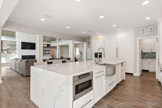 12974 Boulderway Trl, Grand Haven, MI 49417 - kitchen featuring wood finished floors, a center island with sink, white cabinets, a stone fireplace, and light stone counters