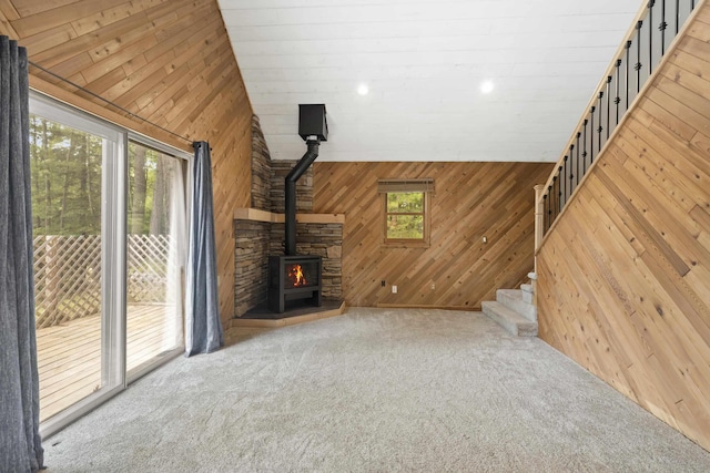 4382 S Vandervoight, Traverse City, MI 49696 - unfurnished living room featuring wooden walls, healthy amount of natural light, a wood stove, carpet floors, and lofted ceiling