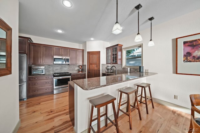 4078 Woodland Ave, Manitou Beach, MI 49253 - kitchen featuring appliances with stainless steel finishes, a breakfast bar, backsplash, light wood finished floors, and glass insert cabinets