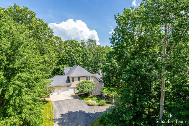 5264 Deverman Ct NE, Lowell, MI 49331 - view of property hidden behind natural elements featuring asphalt driveway, a wooded view, and a garage