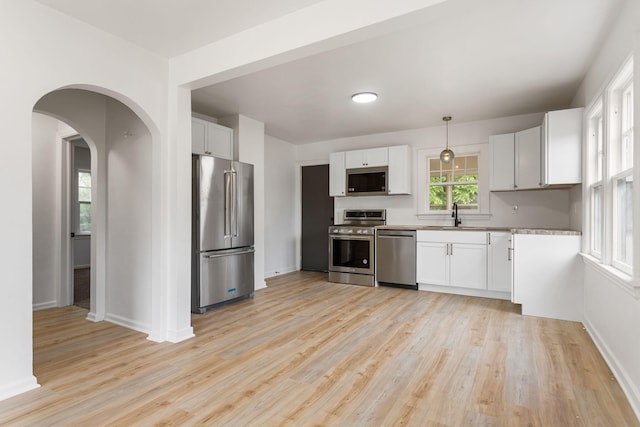 1680 Kalamazoo Ave SE, Grand Rapids, MI 49507 - kitchen featuring appliances with stainless steel finishes, light wood-style floors, white cabinetry, arched walkways, and decorative light fixtures