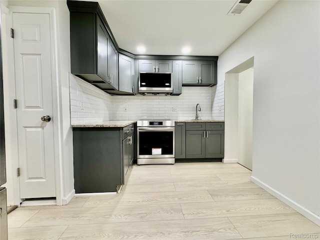 4915 Clarkston Rd, Clarkston, MI 48348 - kitchen featuring stainless steel appliances, light wood-style floors, tasteful backsplash, and light stone counters