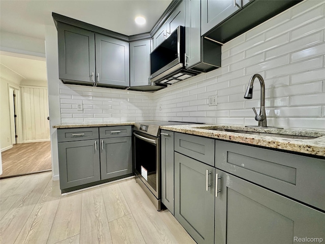 4915 Clarkston Rd, Clarkston, MI 48348 - kitchen featuring appliances with stainless steel finishes, gray cabinetry, light wood-style flooring, light stone counters, and tasteful backsplash
