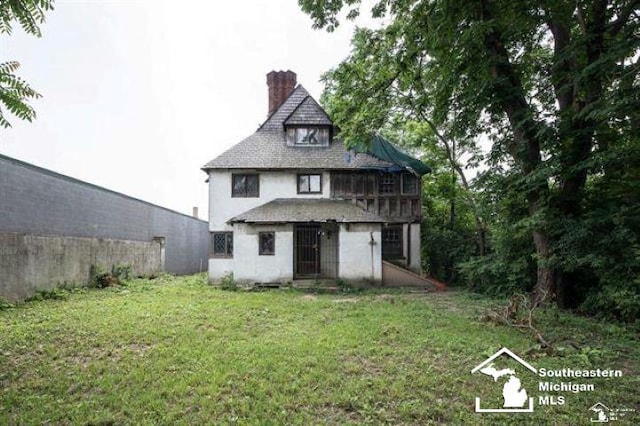 1989 W Grand Blvd, Detroit, MI 48208 - rear view of house with a chimney, stucco siding, a lawn, and a shingled roof
