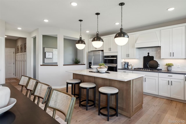 873 Risdon Trl S, Saline, MI 48176 - kitchen featuring stainless steel appliances, premium range hood, a center island, a kitchen breakfast bar, and light wood finished floors