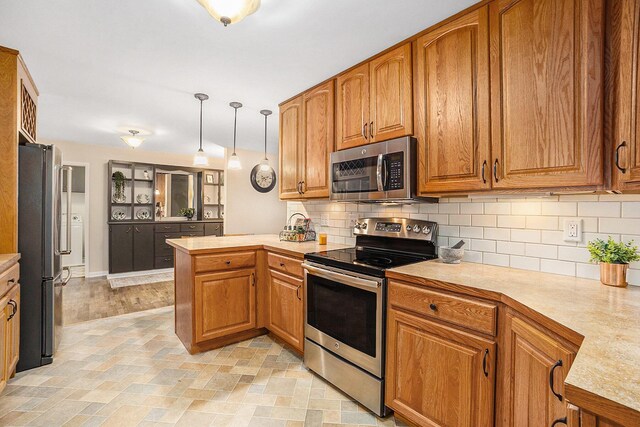 308 N Thomas St, Scottville, MI 49454 - kitchen with appliances with stainless steel finishes, a peninsula, light countertops, brown cabinets, and decorative backsplash