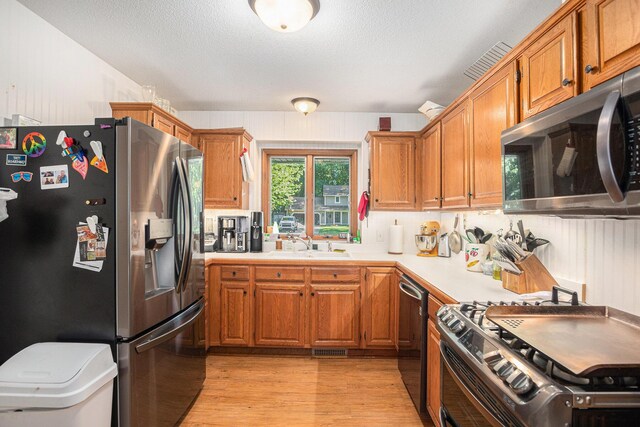 15303 Arborwood Dr, Grand Haven, MI 49417 - kitchen with stainless steel appliances, light countertops, light wood-type flooring, brown cabinets, and a textured ceiling