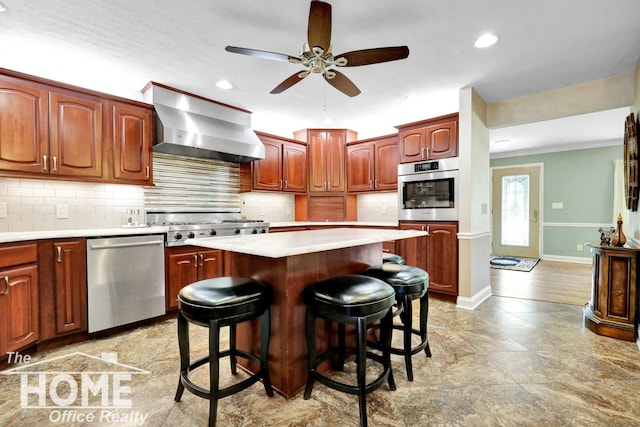 2367 Meadowdown Dr, Owosso, MI 48867 - kitchen featuring stainless steel appliances, wall chimney exhaust hood, a ceiling fan, light countertops, and a kitchen island