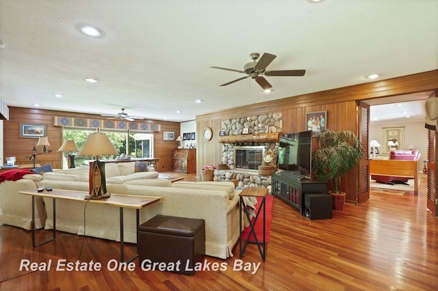 1360 Delta Dr, Saginaw, MI 48638 - living room featuring a ceiling fan, wood finished floors, wood walls, a stone fireplace, and recessed lighting