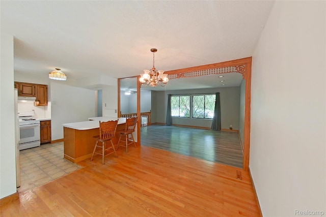 11589 Lombardy Ct, Pinckney, MI 48169 - kitchen featuring white gas range oven, light countertops, a chandelier, under cabinet range hood, and light wood finished floors