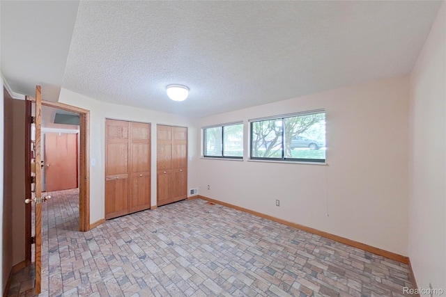 11589 Lombardy Ct, Pinckney, MI 48169 - unfurnished bedroom with multiple closets, brick patterned flooring, and a textured ceiling