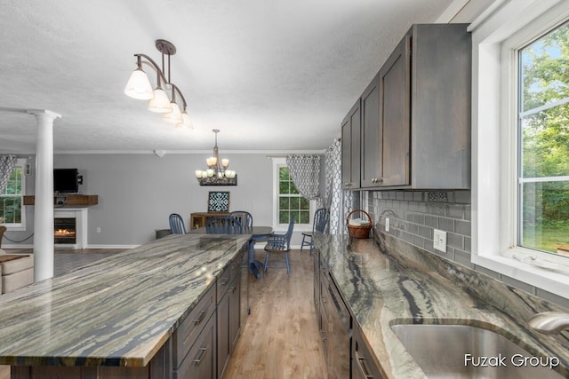 3268 Michele Ln, Hamilton, MI 49419 - kitchen featuring dark stone counters, light wood-type flooring, a lit fireplace, backsplash, and pendant lighting