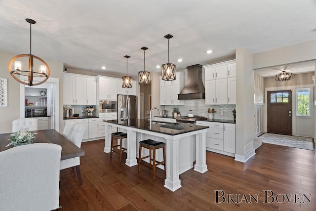 9633 Waterstone Dr, Byron Center, MI 49315 - kitchen with wall chimney exhaust hood, a chandelier, dark countertops, stainless steel appliances, and dark wood-style floors