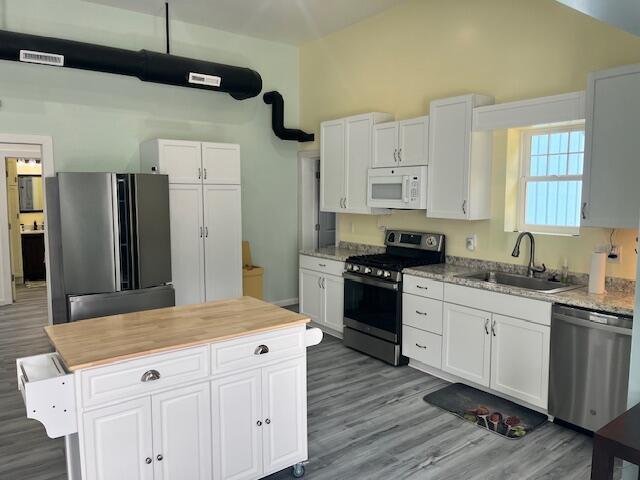 4969 N Highbridge Rd, Brethren, MI 49619 - kitchen featuring appliances with stainless steel finishes, white cabinetry, wood finished floors, vaulted ceiling, and a center island